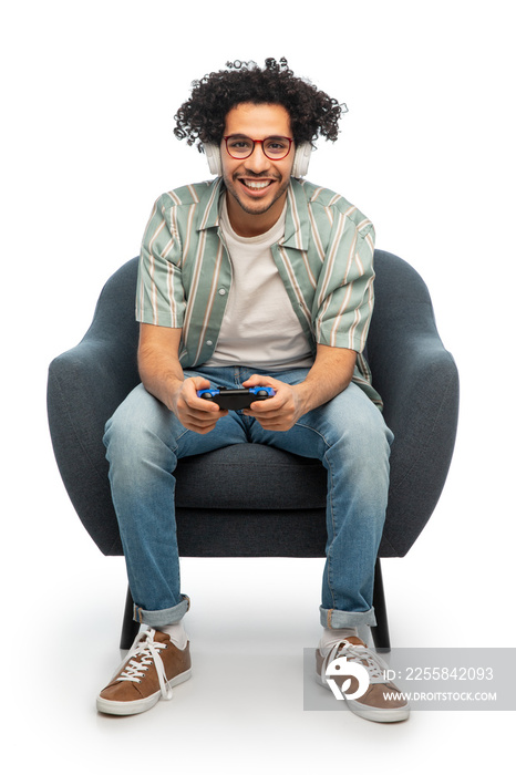 technology, people and leisure concept - happy smiling young man in headphones with gamepad sitting 