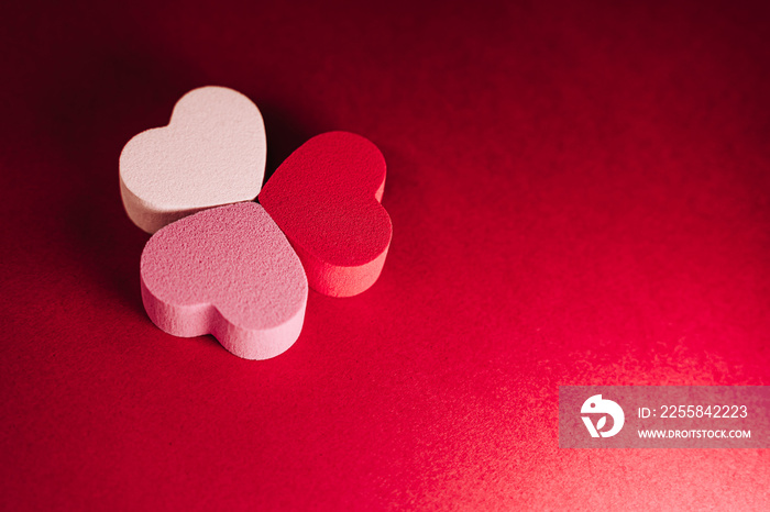 Top view of a three little hearts of sponges on a red background. There are one white heart, one pin