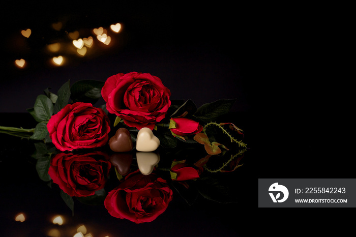 Red roses and heart shaped chocolate on black background