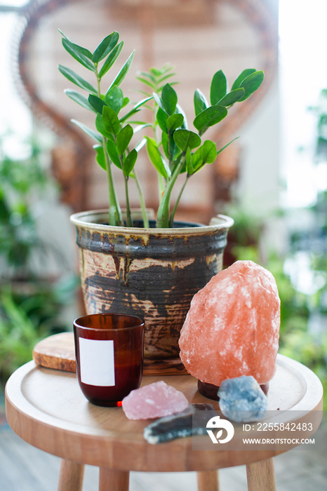 a plant, a salt lamp, a candle and crystals on a wooden chair in a bright room