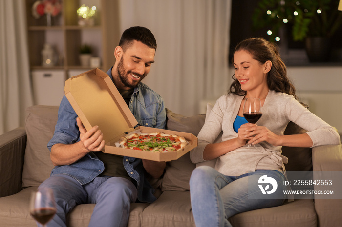 leisure, people and fast food concept - happy couple with wine eating takeaway pizza at home in even