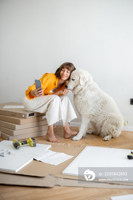 Young woman makes selfie photo on phone with her cute dog, have fun while making repairing at new ap