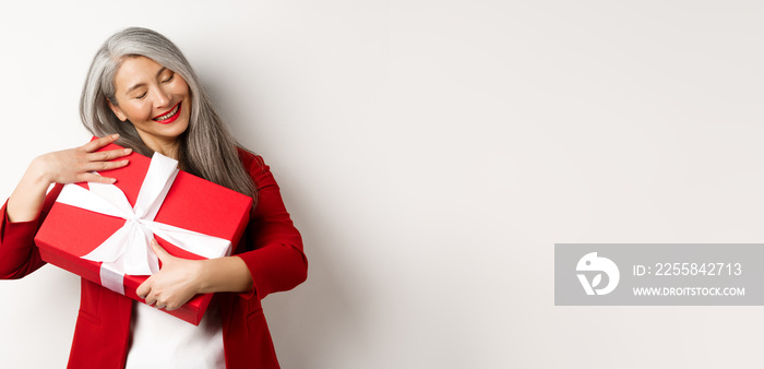 Valentine day concept. Beautiful asian senior woman hugging box with gift, smiling and looking happy