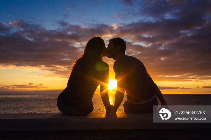 Man and woman sitting by the sea kiss at sunset at Meloneras beach walk, Gran Canaria. Couple silhou