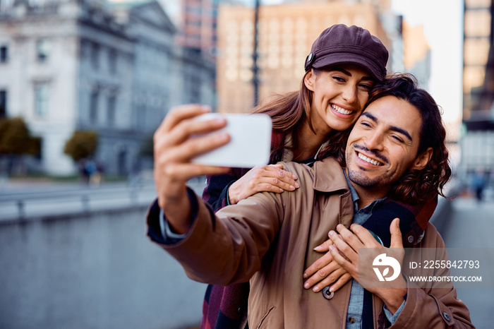 Happy Hispanic man and his girlfriend having fun while talking selfie with cell phone in city.