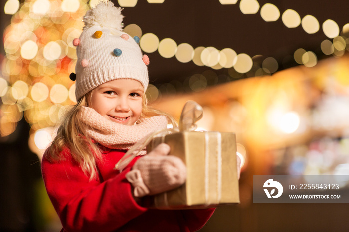 holidays, childhood and people concept - happy little girl with gift box at christmas market in wint