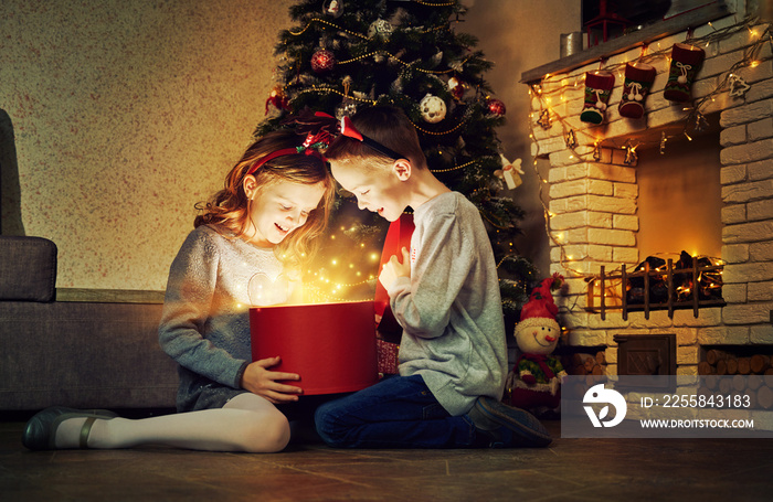 Happy kids with magic gift box at home near christmas tree and fireplace. Merry Christmas time and f