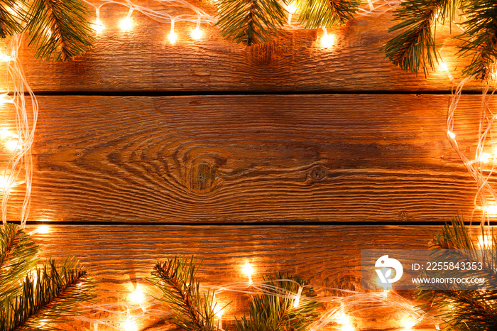 Image of wooden surface with burning garland around perimeter, branches of spruce.