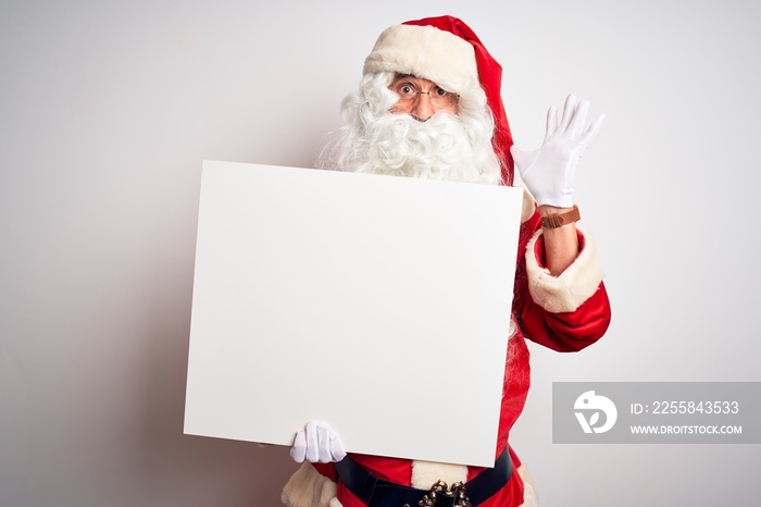 Middle age man wearing Santa Claus costume holding banner over isolated white background very happy 