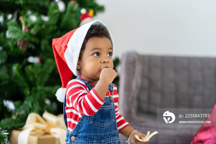 Cute African American little boy wearing red Santa hat eating and playing with decoration items for 