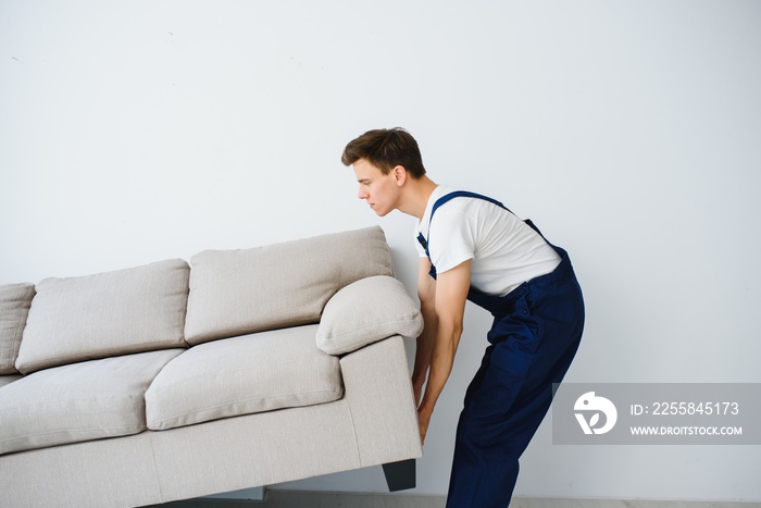 Loader moves sofa, couch. worker in overalls lifts up sofa, white background. Delivery service conce