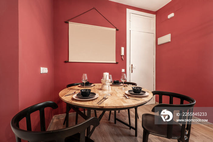 Apartment with round wooden dining table, food service, black chairs, white door and red walls