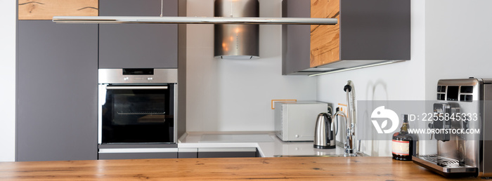 Modern kitchen interior with lights on. Brown wooden table and bar stools, coffee machine. Contempor