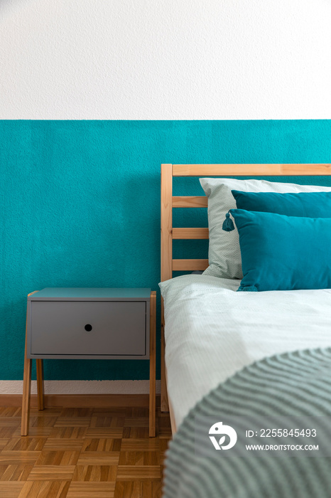 Detail of wooden bed with turquoise wall and many pillows on the sheets