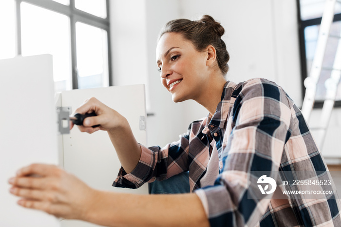 repair, improvement and furniture concept - happy smiling woman with screwdriver assembling locker a