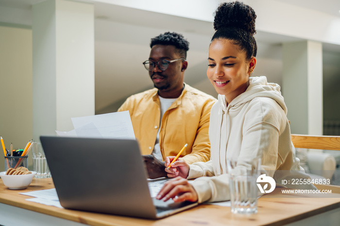 Diverse couple using laptop while sitting at the table at home