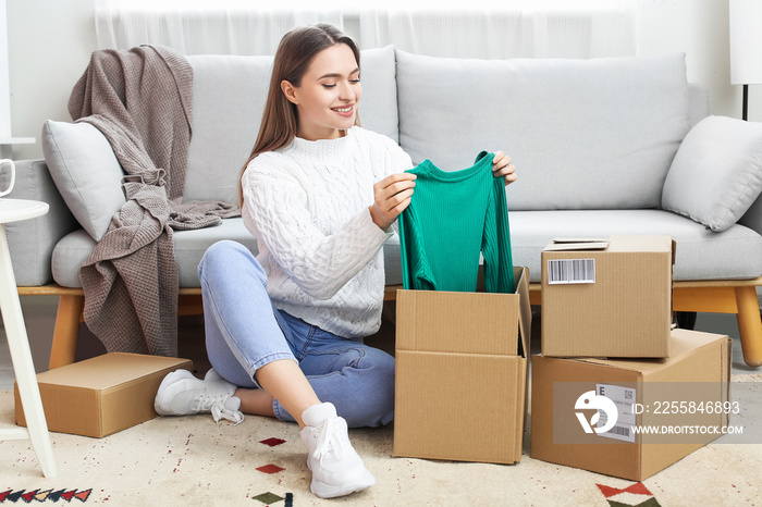 Young woman opening parcel with new clothes at home