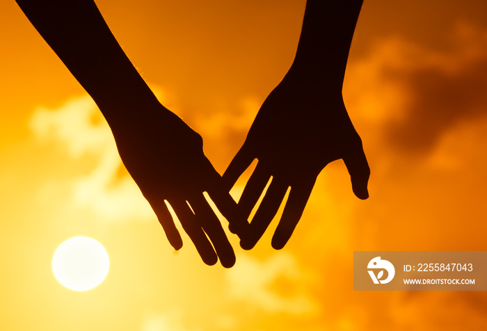 Man and womans hand coming together against beautiful sunset.