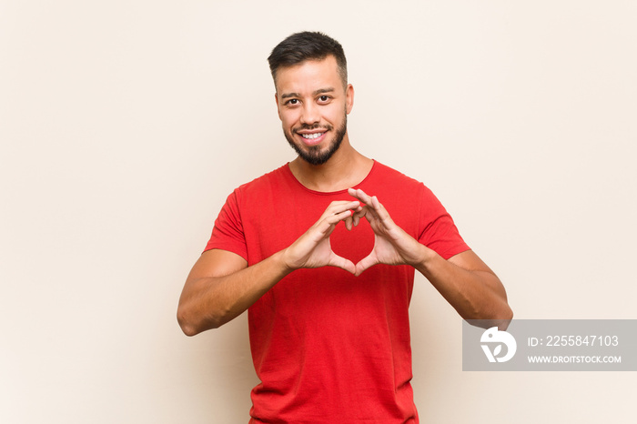 Young south-asian man smiling and showing a heart shape with hands.