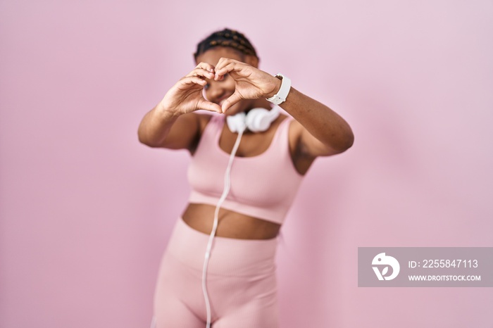 African american woman with braids wearing sportswear and headphones smiling in love doing heart sym