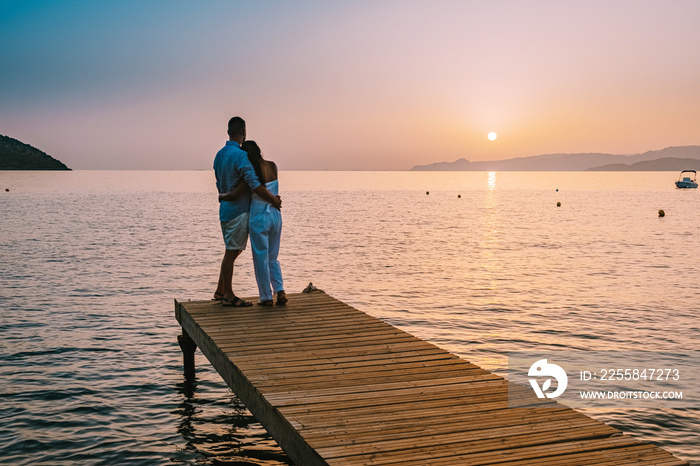 young romantic couple in love is sitting and hugging on wooden pier at the beach in sunrise time wit