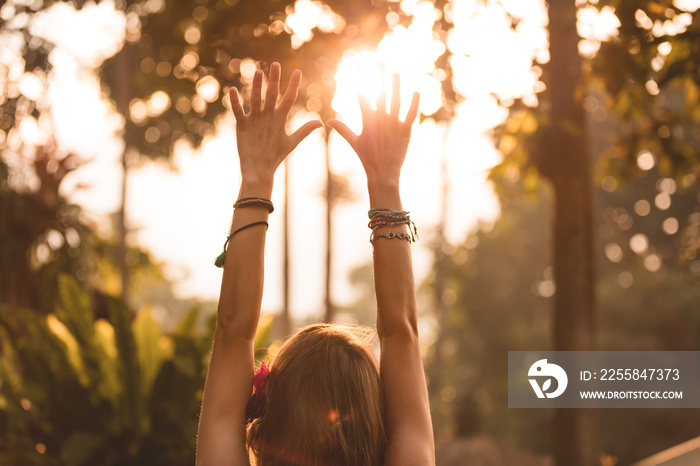 Woman holding hands in the air with orange sunlight in the background.