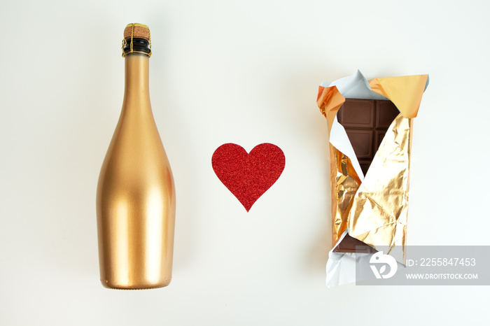 Golden champagne bottle and chocolate bar in gold wrapper and red glitter heart on a white backgroun
