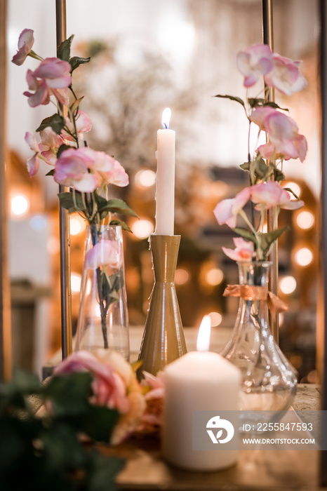 Beautiful gold candle stick lit flame burning bright surrounded by lights and flowers behind. Romant