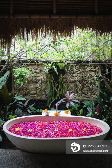 Luxury hotel bathroom with red and pink tropical flowers, spa concept  Bathtube with petals in tropi