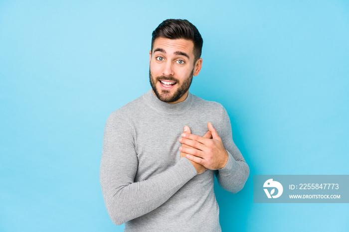 Young caucasian man against a blue background isolated has friendly expression, pressing palm to che