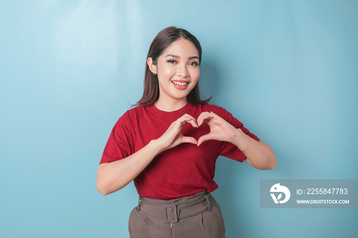 An attractive young Asian woman wearing a red t-shirt feels happy and a romantic shapes heart gestur