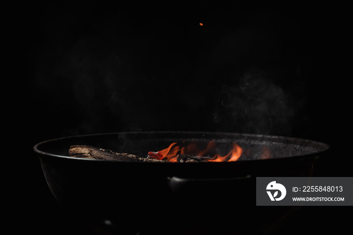 Firewood burns in a round barbecue at night. Dark background. Preparing to cook food on the grill.