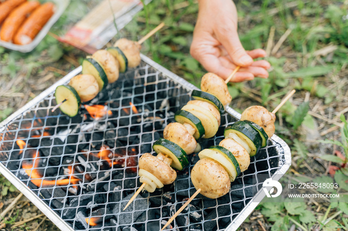 Close up of single use grill for outdoors picnic with vegetables on wooden stick.