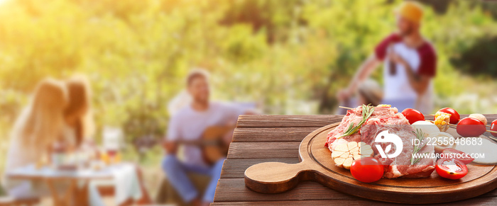 Board with raw meat and vegetables for barbecue party on wooden table outdoors