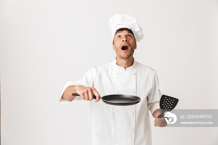 Young chef man standing isolated over white wall background holding frying pan cooking.
