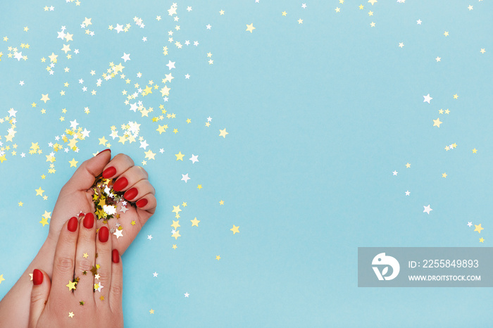 Woman hands with red manicure on blue background with golden stars sprinkles.