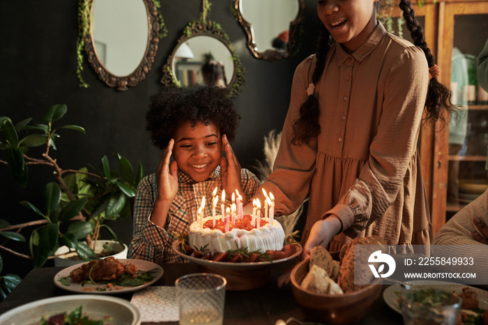 African little boy looking at birthday cake with excitement at table while celebrating birthday with