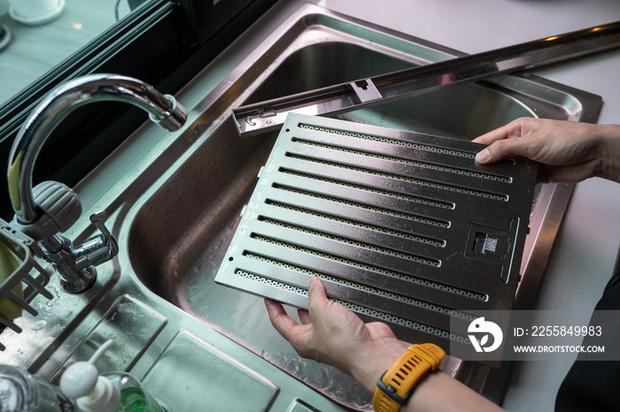 Woman hands holding a cooker hood filters for cleaning it at sink. Clean your filters every two to t