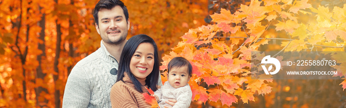 Asian Chinese mother and Caucasian father dad with baby girl in autumn fall park. Family together outdoor in nature. Seasonal holiday and authentic lifestyle. Banner header for a website.