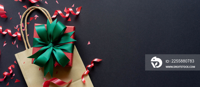 close up top view of christmas gift box with shopping bag with red rolling ribbon and confetti on black background with copy space for black Friday season and happy new year festival concept