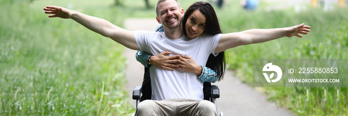 Woman hugs joyful man in wheelchair in park