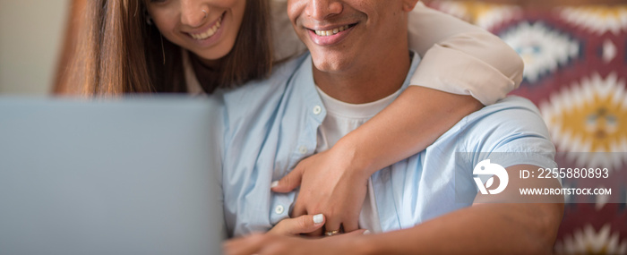 Banner image of black and caucasian man and woman working happy together with a laptop at home hugging with love and relationship. Young couple living together and work on computer. Modern people