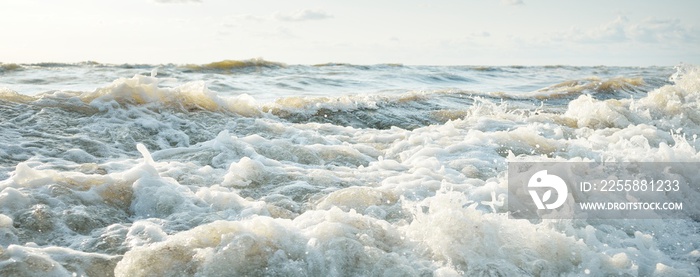 Baltic sea shore after the storm. Sunset, soft golden sunlight. Water surface texture, crashing waves and splashes, foam. Picturesque panoramic scenery. Idyllic seascape. Nature, environment, ecology