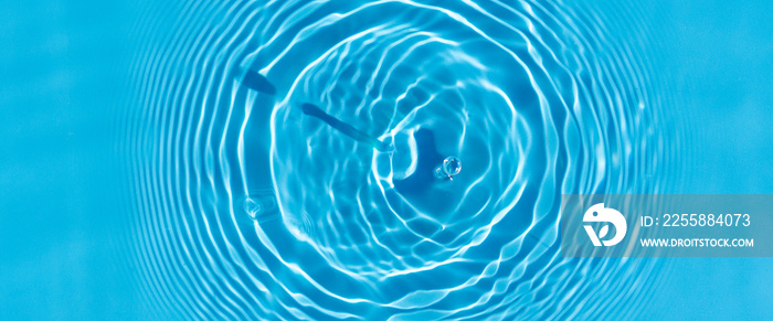 Wave from a drop of water on blue water under natural light. Top view, flat lay.