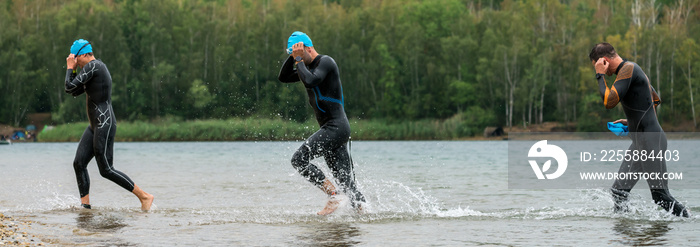 Three triathletes in wetsuits running out of the lake after finishing the swim