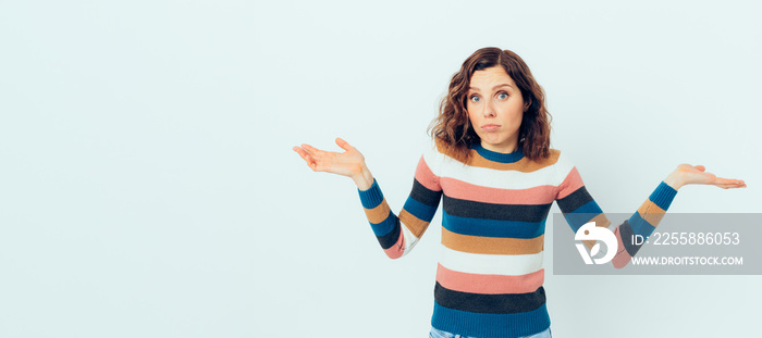 Confused young woman with brown curly hair shrugs her shoulders