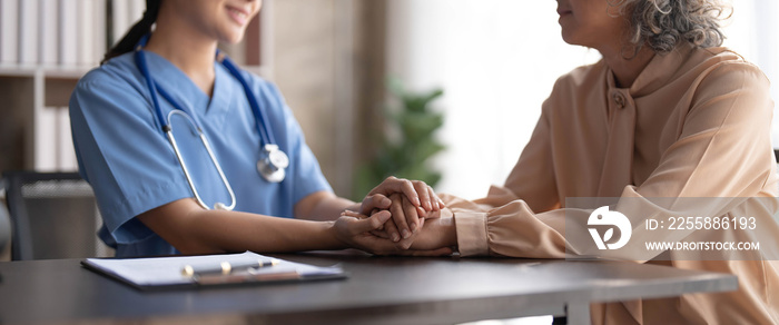 Happy patient is holding caregiver for a hand while spending time together. Elderly woman in nursing home and nurse