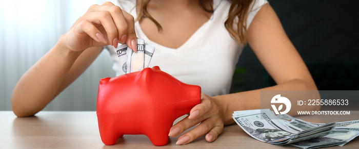 Young woman putting money into piggy bank on table