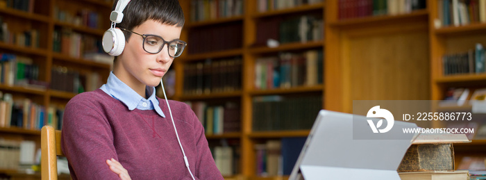 Young woman studying in the library using laptop and headphones