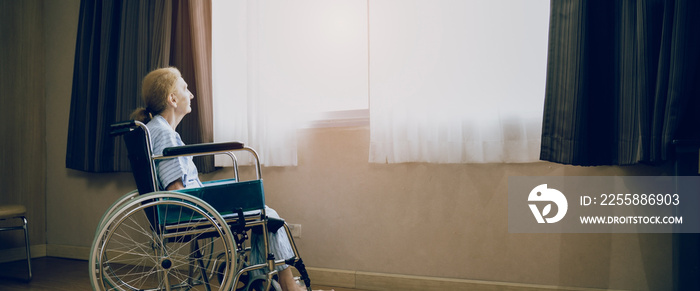 Retirement and Lonely women concept.Panoramic caucasian elderly woman in wheelchair while looking out the window in nursing home or hospital.